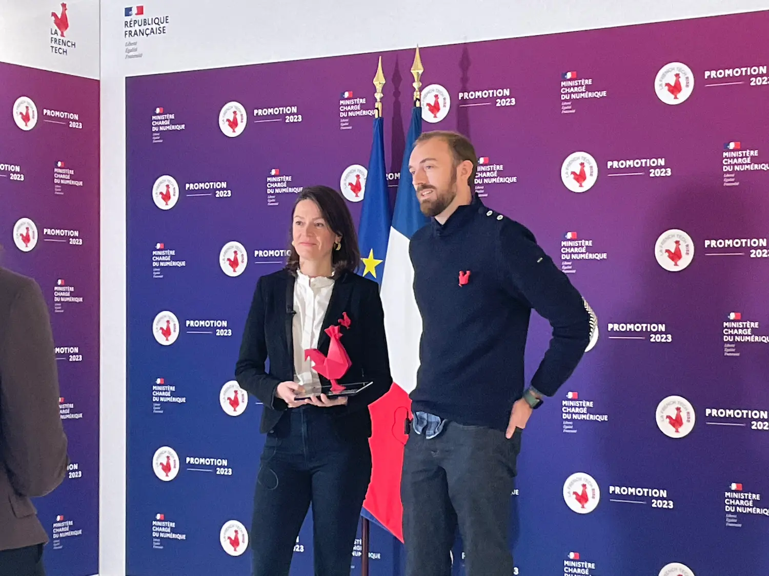 Two members of the team at the French Tech Promotion 2023 ceremony, holding the red rooster trophy in front of the Ministry for Digital Affairs backdrop.